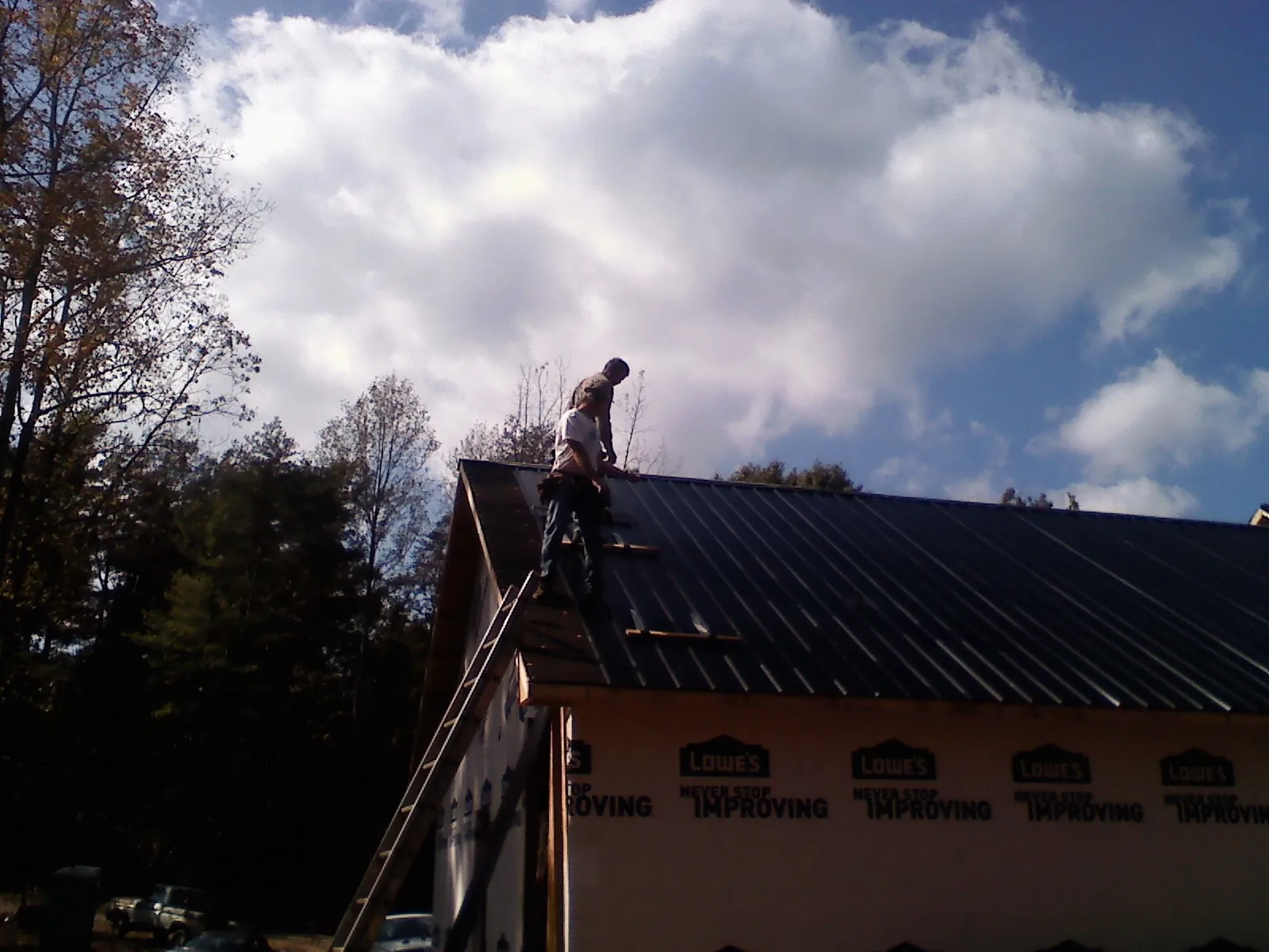 Roofer fastening dark metal panels high against a cloudy sky, from a Roof Inspection job in Collins